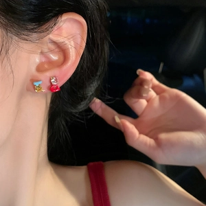 Exquisite macro detail of asymmetric colorful zircon stud earrings worn by a woman