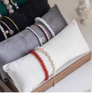 Macro shot of pearl and agate bracelets displayed on soft velvet pillows in wooden tray