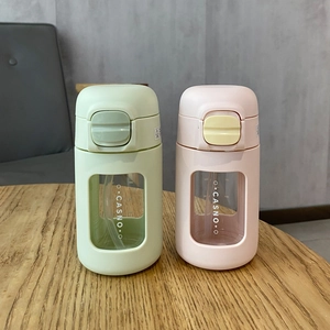 Dual portable glass cups with straw and lids in light green and pink on a wood table