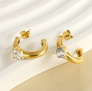 Detail of C-shaped gold earrings with heart-cut crystals on elegant satin fabric