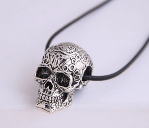 Close-up of vintage silver skull pendant with detailed engravings on a black cord