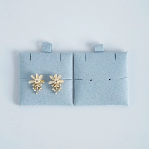 Detail of flower earrings with white pearls and rhinestones on light blue velvet card
