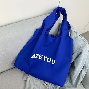 Blue canvas tote bag with AREYOU lettering displayed on a grey sofa with a denim jacket