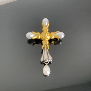 Macro detail of baroque cross pendant featuring white pearls and a golden matte finish