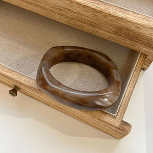 Detail of amber marble resin bangle displayed in a wooden drawer with fabric lining