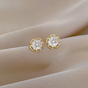 Macro detail of gold flower earrings with white zircons on champagne silk fabric