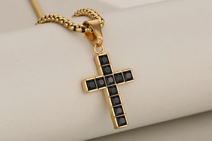 Close-up of gold-plated cross pendant with black cubic zirconia stones on box chain