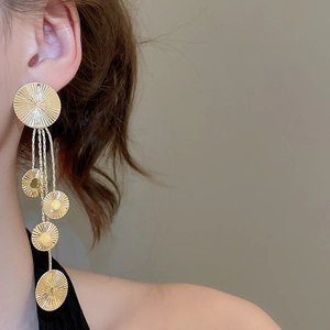 Detailed view of long gold tassel earrings with radial textured geometric round discs