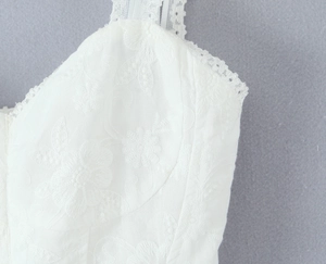 Close-up of white floral embroidery and delicate lace trim on a slim fit camisole top
