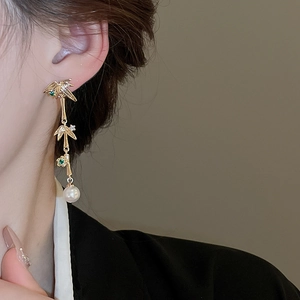 Detail of elegant gold drop earring with green zircon and pearl worn on model