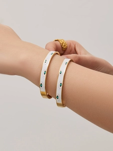 Close-up of white enamel Evil Eye bangles and a gold sunflower ring on a model's wrist