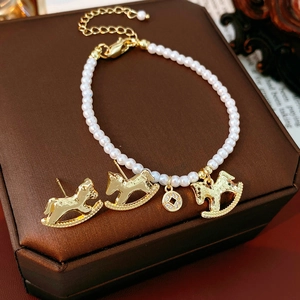 Detailed macro view of gold rocking horse charms and white pearls on a minimalist bracelet