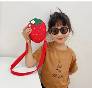 Girl wearing a red strawberry shaped crossbody bag with gold studs and floral details