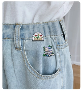 Detailed view of floral book enamel pins on denim jeans with Grow Your Mind text
