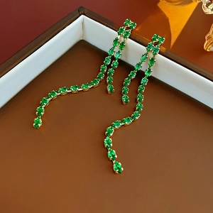 Close-up of elegant gold tassel earrings with green crystal drop on leather texture