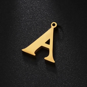 Macro shot of gold letter A stainless steel pendant with crystal accents on dark surface