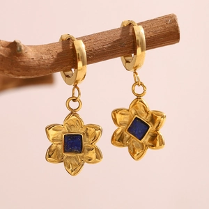 Close-up of 18K gold flower earrings with blue gemstone on a wooden branch
