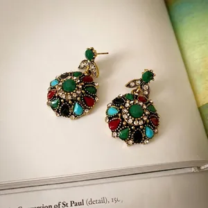 Vintage gold medal earrings with green stone and colorful crystals on book pages