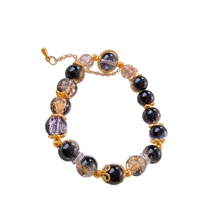 Beaded bracelet with purple and amber beads and golden metal charms on white background