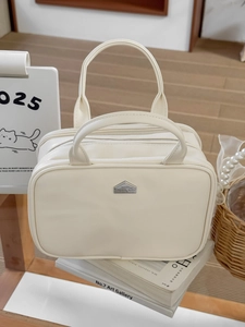 Detail of cream PU leather makeup bag with dual zippers and house-shaped logo metal plate