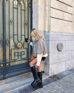 Outdoor street style view of woman in grey knitted cape with white top and tall boots