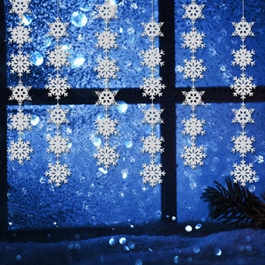 White snowflake string ornaments hanging in front of a blue winter bokeh background