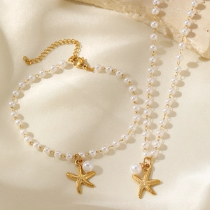 Elegant gold starfish charm pearl necklace and bracelet set on yellow silk background