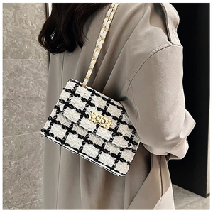 Detail of elegant black and white tweed chain bag worn with a stylish trench coat
