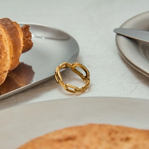 Dettaglio anello a catena dorata con zirconi su un tavolo da colazione elegante