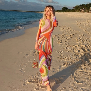 Detail of long-sleeved floor-length dress with colorful wave print on a beach at sunset