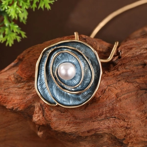 Detail of a gold rose pendant with blue enamel and a pearl on a rustic wood background
