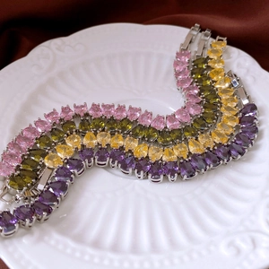 Detailed view of pear-cut zircon bracelets in pink, green, yellow, and purple on a ceramic plate