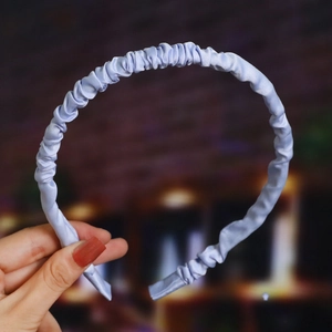 Close-up of light blue pleated satin headband held by hand with a soft indoor glow