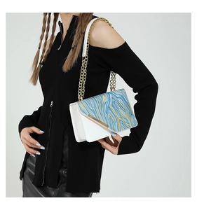 Close-up of white shoulder bag with blue gold wave pattern and elegant gold chain strap