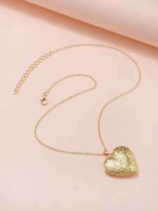 Detail showing a golden heart locket with floral engraving on a soft pink backdrop