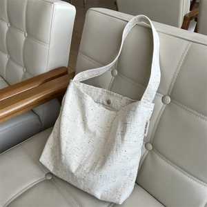 Dettaglio della borsa tote in tela crema con puntini colorati ed etichetta laterale del brand