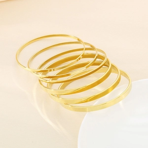 Close-up of stacked 18k gold plated stainless steel bangles set on a minimalist background