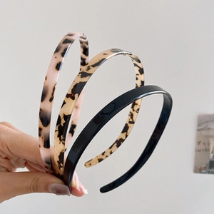 Close-up of three thin headbands in pink leopard, brown leopard, and solid black colors