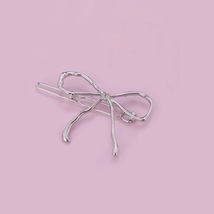 Sleek silver metal bow hair clip with minimalist irregular fluid design on purple background