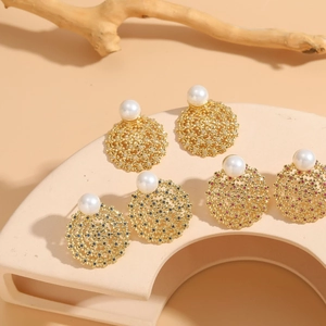 Detailed close-up of hollow gold zircon pearl earrings set on minimalist geometric display