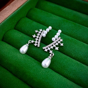 Detailed close-up of zircon crown earrings with teardrop pearls on green velvet