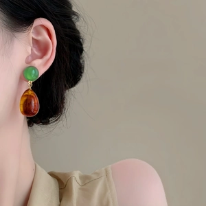Asymmetric resin teardrop earrings in green and amber colors worn by a model