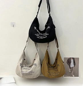 Trois grands sacs fourre-tout en toile noir, beige et kaki suspendus sur un mur d'exposition