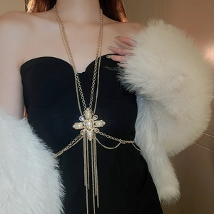 Detailed view of layered gold body chain with pearl cross pendant and tassel fringe