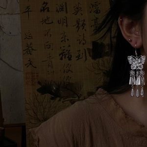 Close-up of silver butterfly earrings with metal tassels against a bamboo background