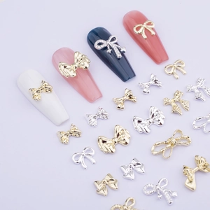 Detailed view of silver and gold metal bow nail art charms on white nails