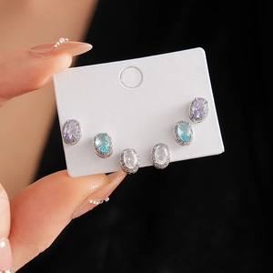 Three pairs of oval zircon halo stud earrings in purple, blue, and clear on display card