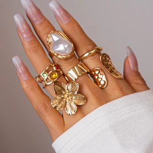 Detailed view of layered gold flower rings and baroque pearl accents on a hand