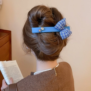 Close-up of blue checkered bow hair clip with orange smiley flower and crystal on hair