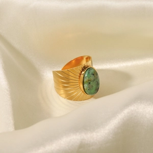 Close-up of golden wide band ring with green oval stone on soft beige silk fabric